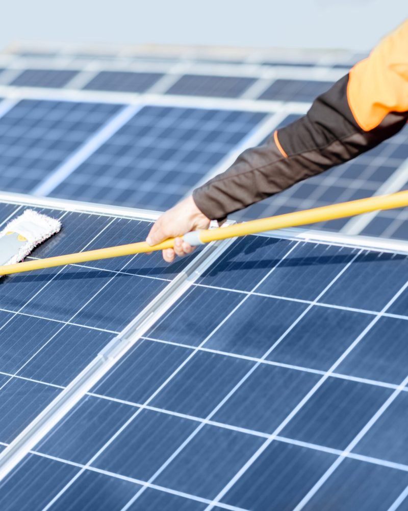 Professional cleaner in protective workwear cleaning solar panels with a mob. Concept of solar power plant cleaning service